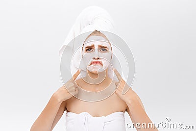 Unhappy beautiful young woman with white clay face mask makes acne therapy, wears white towel on hair, posing against Stock Photo