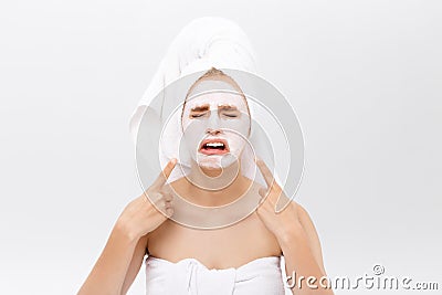 Unhappy beautiful young woman with white clay face mask makes acne therapy, wears white towel on hair, posing against Stock Photo