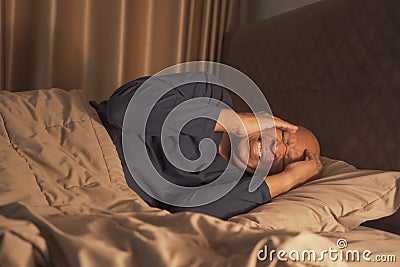 Unhappy black man. African American person is terrified from disturbing nightmare, sleeping with stress on bed in bedroom at home Stock Photo