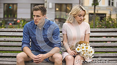 Unhappy couple sitting after fight, girl with flowers, problem in relationship Stock Photo