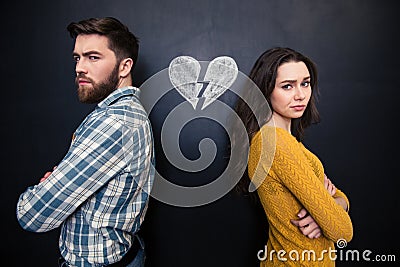 Unhappy couple standing over chalkboard background with drawn broken heart Stock Photo