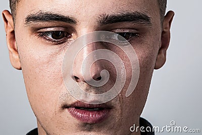 Unhappy crying young man with dropping tears on the face. Closeup studio portrait on grey background. Negative concept Stock Photo