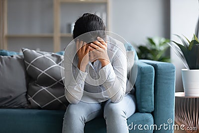 Unhappy depressed Indian woman holding head in hands, sitting alone Stock Photo