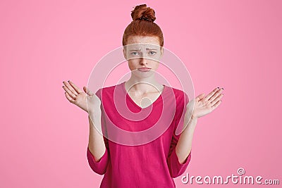 Unhappy displeased female model with hair bun, shrugs shoulders in bewilderment, makes questioning gesture, being uncertain, has c Stock Photo