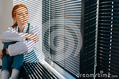 unhappy frustrated female doctor crying sitting near window in sunny day. Stock Photo