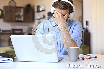 Unhappy frustrated young male holding head by hands sitting with laptop behind desk at home Stock Photo