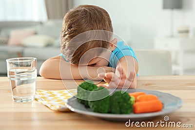 Unhappy little boy refusing to eat vegetables at table Stock Photo