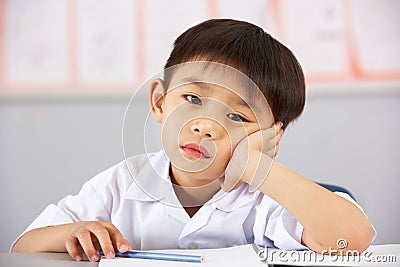 Unhappy Male Student Working At Desk In School Stock Photo