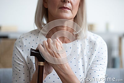 Unhappy mature woman holding hands on walking stick close up Stock Photo