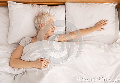 Unhappy old lady looking at empty side of her family bed Stock Photo