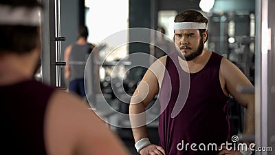 Unhappy overweight man looking at his mirror reflection in gym, diet and sport Stock Photo