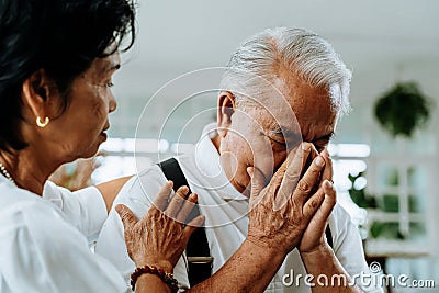 Unhappy retired Asian senior couple sitting on the sofa while elderly wife comforting her sad husband at home. Stock Photo