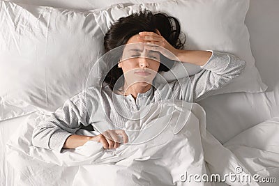 Unhappy sad tired caucasian millennial female lies on bed, suffers from headache, migraine in bedroom Stock Photo