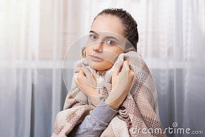 Unhappy sick brunette girl wrapped in blanket suffering from cold at home, looking at camera, freezing, complaining to Stock Photo