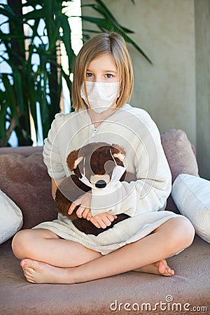 Unhappy sick toddler girl wearing medicine mask for protection sitting with toy teddy bear Stock Photo