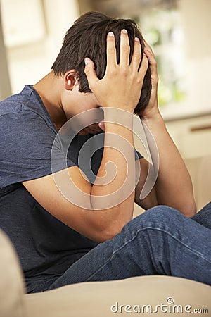 Unhappy Teenage Boy Sitting On Sofa At Home Stock Photo