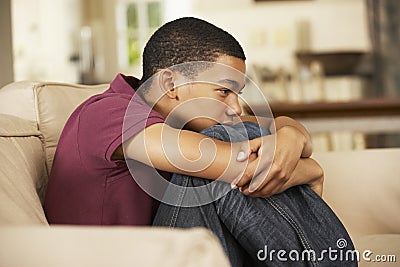 Unhappy Teenage Boy Sitting On Sofa At Home Stock Photo