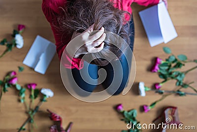 Unhappy woman sitting on the floor among scattered flowers and reading letter. Broken relationships in bad Valentine`s day Stock Photo