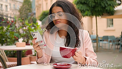 Unhappy young Indian Arabian ethnic woman female girl drinking coffee feel annoyed negative message notification mobile Stock Photo