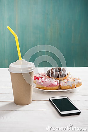 Unhealthy breakfast with coffee to go, plate of frosted donuts and smartphone wth black screen on wooden table Stock Photo