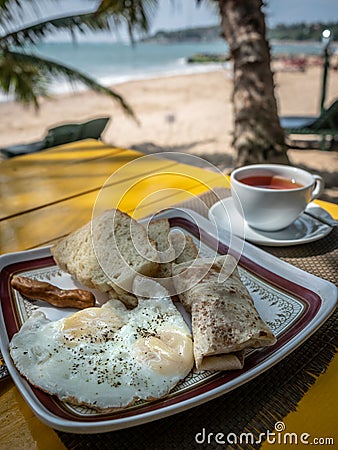 Unhealthy breakfast on the sunny beach. Fried eggs with sausage and bread Stock Photo