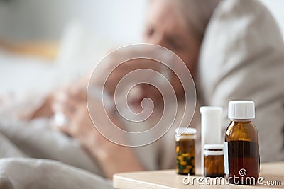 Unhealthy mature woman suffering from cold, meds on bedside table Stock Photo