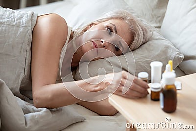 Unhealthy older woman taking pills from bedside table close up Stock Photo