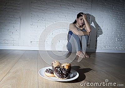 Unhealthy sugar donuts and muffins and tempted young woman or teenager girl sitting on ground Stock Photo