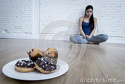 Unhealthy sugar donuts and muffins and tempted young woman or teenager girl sitting on ground Stock Photo