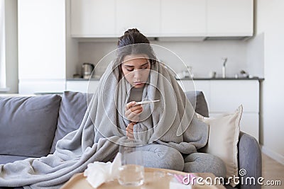 Unhealthy upset young female with fever looking at thermometer with high degree temperature. Stock Photo