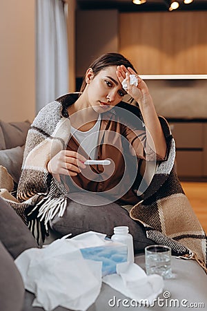 Unhealthy woman sit in blanket hat feel sick suffer from flu or covid-19 corona virus. Unwell young female sneeze sniffle have Stock Photo