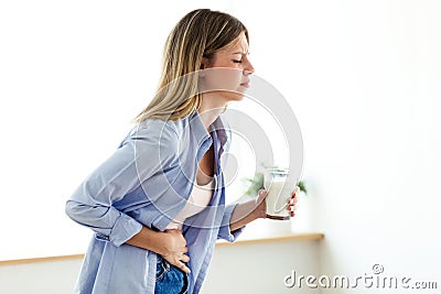 Unhealthy young woman with stomachache holding a glass with milk at home. Stock Photo