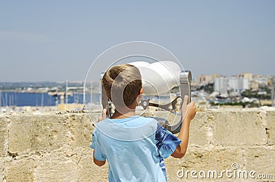 Unidentifiable blond child looks through the binoculars at the sea from Gallipoli castle. Apulia, Italy Editorial Stock Photo