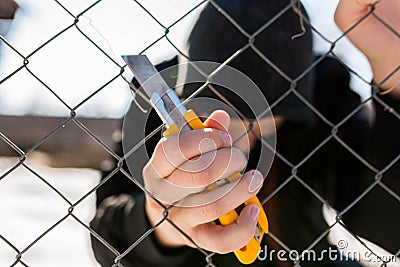 Unidentifiable teenage boy behind wired fence holding a paperknife at correctional institute Stock Photo