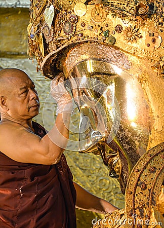 Unidentified Burmese monk is cleaning Buddha statue with the golden paper at Mahamuni Buddha temple, August Editorial Stock Photo