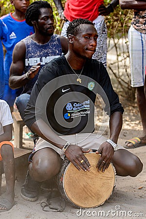 Unidentified Diola man plays on drums in Kaschouane village. Di Editorial Stock Photo