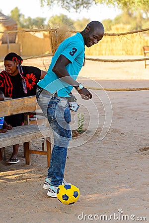 Unidentified Fulani man in jeans and blue shirt plays football Editorial Stock Photo