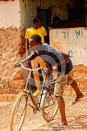 Unidentified local man pulls a bicycle in a village in Guinea B Editorial Stock Photo