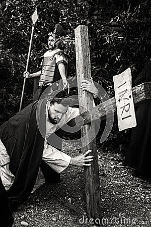 Unidentified man portraying Jesus Christ carries large wooden cross during reenactment of the Crucifixion. Black and White Editorial Stock Photo