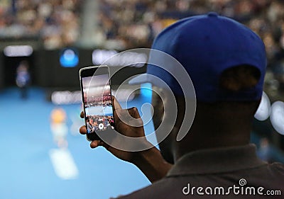 Unidentified spectator uses his cell phone to take images during tennis match at 2019 Australian Open in Melbourne Park Editorial Stock Photo