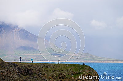 Unidentified tourists standing at the cliff near Gatklettur Stone Arch, Iceland Editorial Stock Photo