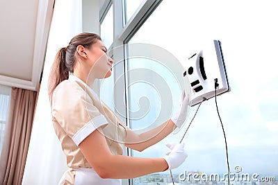 A uniformed maid installs a window cleaner robot on the glass. Clean windows. Photos in the interior. The concept of Stock Photo