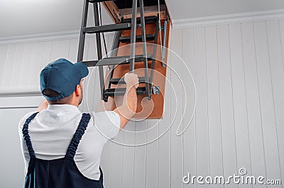 A uniformed specialist lays out the attic ladder after installation Stock Photo