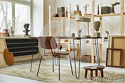 Unique artist workspace interior with stylish desk, wooden easel, bookcase, artworks, painting accessories, decoration. Stock Photo