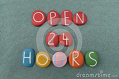 Open 24 Hours, commercial slogan or sign composed with handmade multi colored stone letters over green sand Stock Photo
