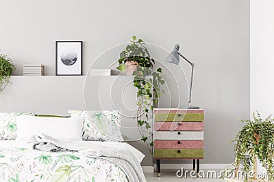 Unique suede covered nightstand with grey lamp in bright scandinavian bedroom with urban jungle, copy space on the empty grey wall Stock Photo
