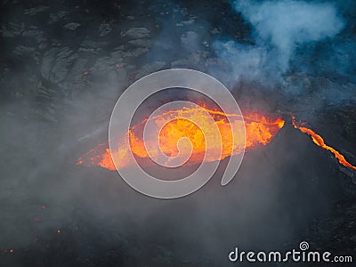 Erupted volcano and surroundings, boiling lava flowing, pull away drone shot Stock Photo