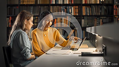 University Library: Two Gifted Girl Students Study, Use Laptop Computer, Help Each Other with Advi Stock Photo