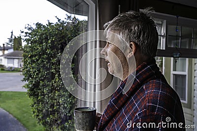 Unkept older man with bed head in housecoat looking out window Stock Photo