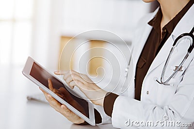 Unknown female doctor using tablet computer in sunny clinic. Perfect medical service in hospital Stock Photo